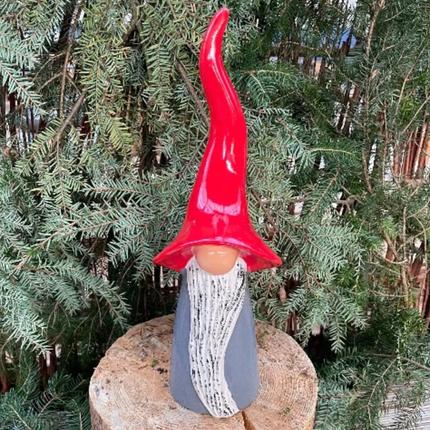 Lifestyle picture showing a grey gnome sitting on a log with foliage of an evergreen tree as a backdrop from Goose and Company.